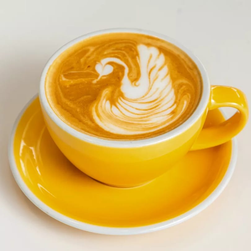 A vibrant yellow coffee cup and saucer with latte art depicting a swan.